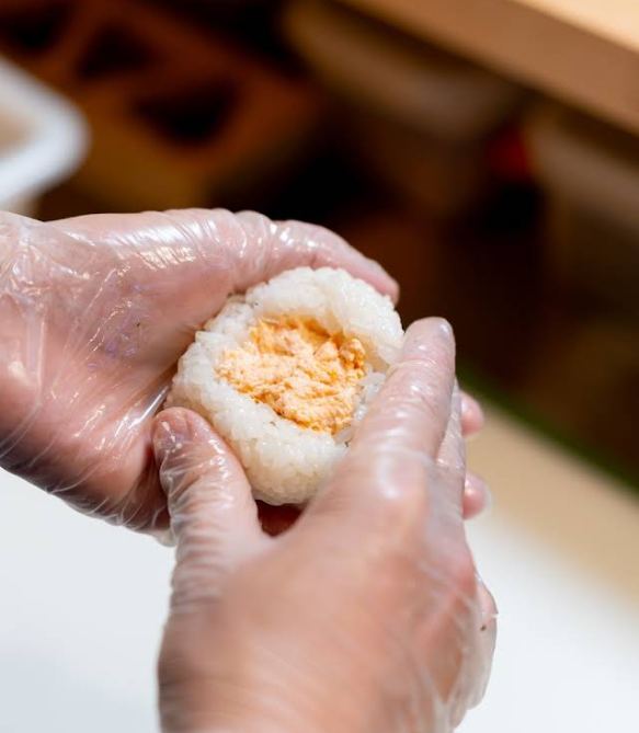 Manos con guantes dando forma a un onigiri relleno de salmón
