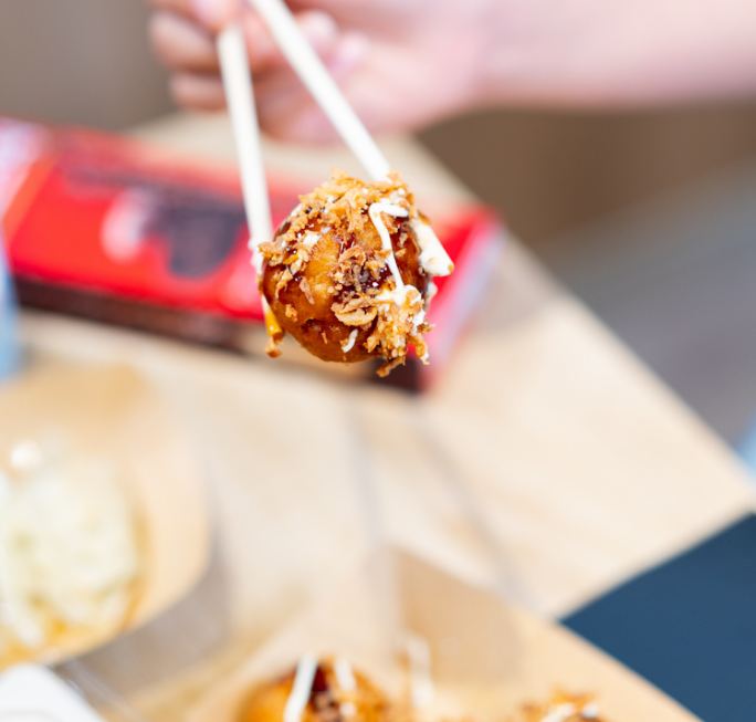 Takoyaki con salsa y bonito seco sujeto con palillos